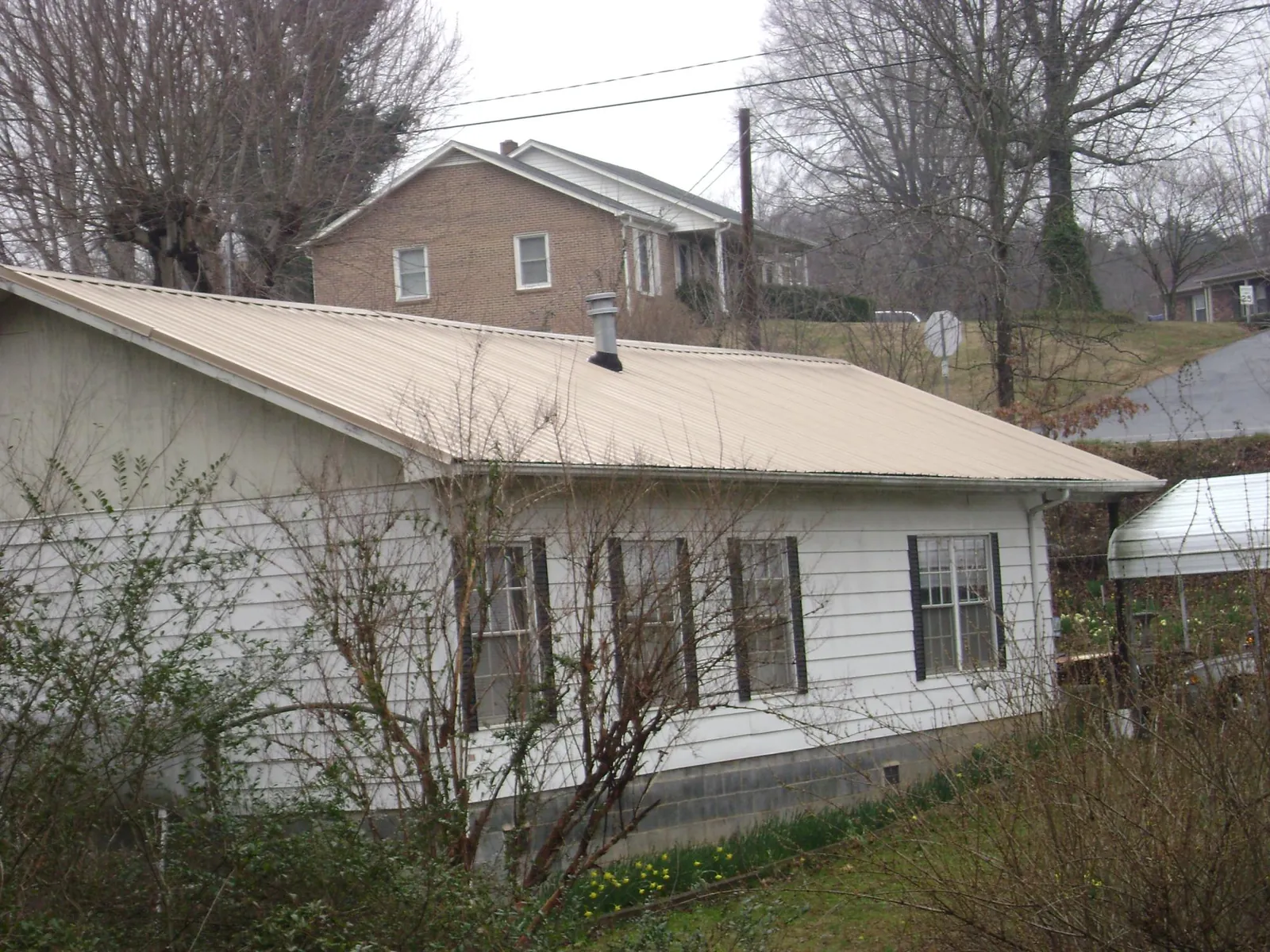 Tan metal roof on a white sided house set into a hillside — Commercial Roofing by Roofing Brothers in Toppenish